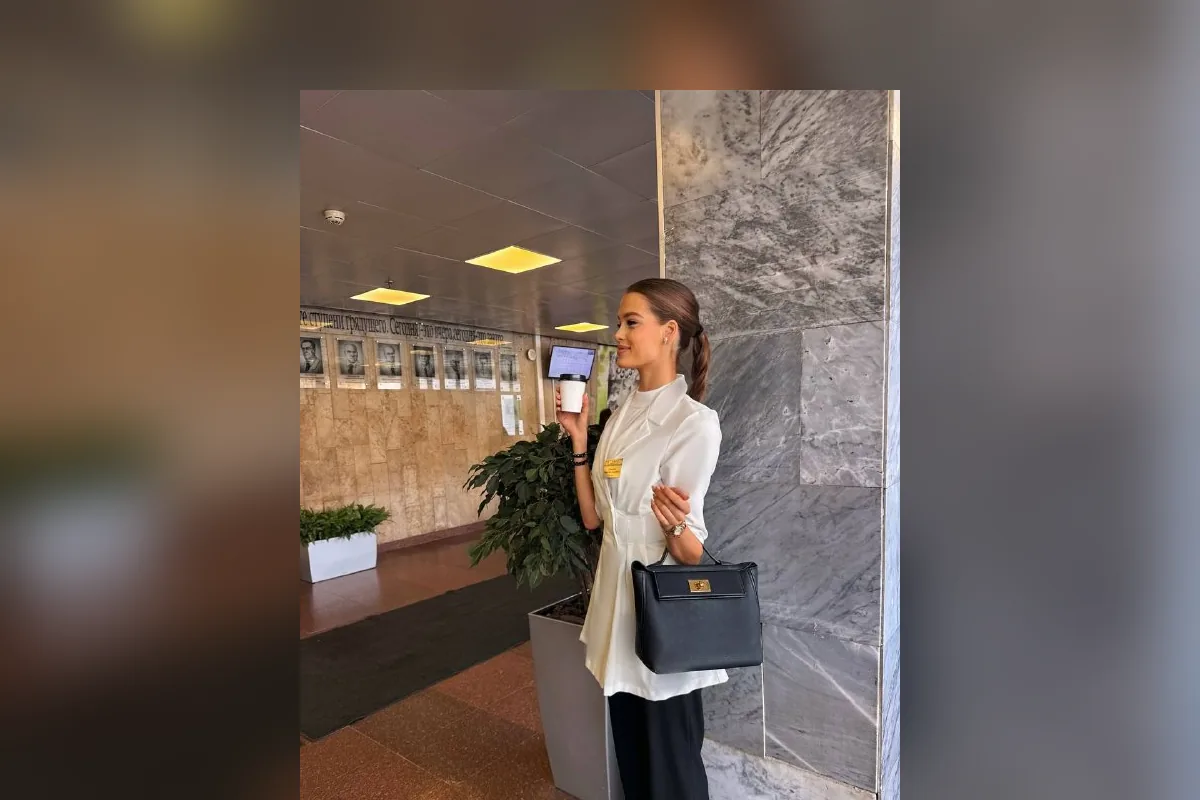 Валентина Алексеева в белом костюме с кофе и сумкой в холле